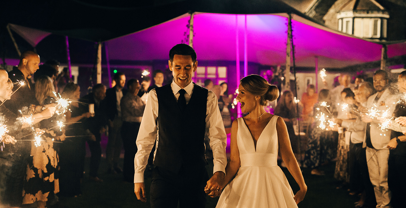 Couple walking under canopy at night, surrounded by people with sparklers.