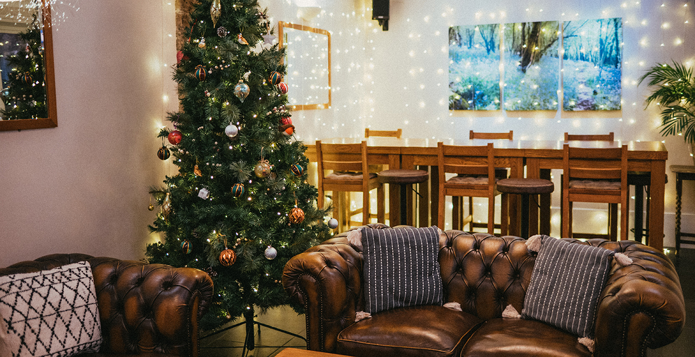 Cosy room with a Christmas tree, leather sofas, and a dining area with fairy lights and artwork.