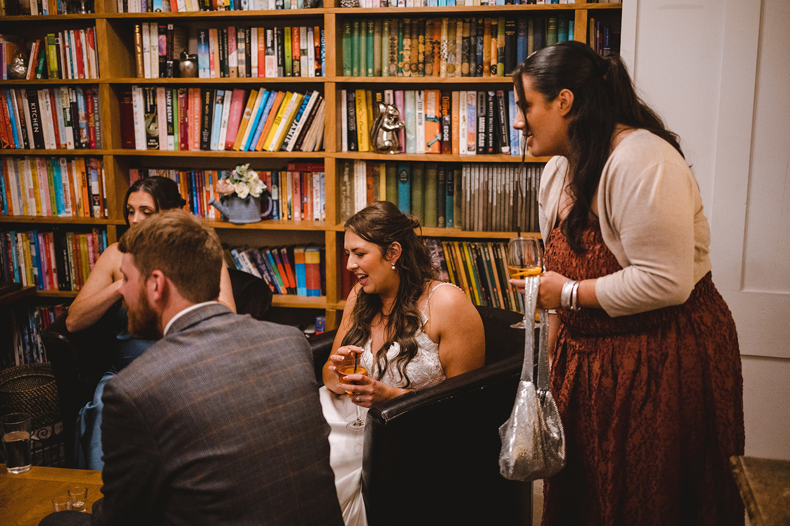 Caer Llan Four people socialising with drinks in a room lined with a large bookshelf filled with books.